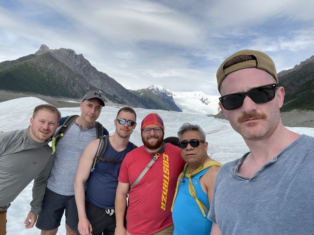 Six men on a glacier with mountains behind them