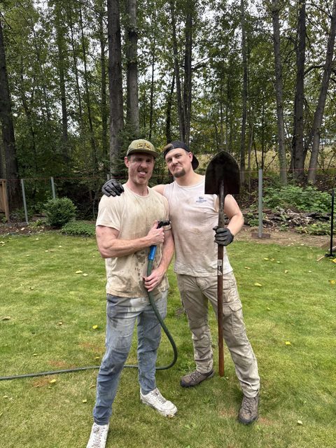 Sean and Derek covered in mud, holding a hose and a shovel