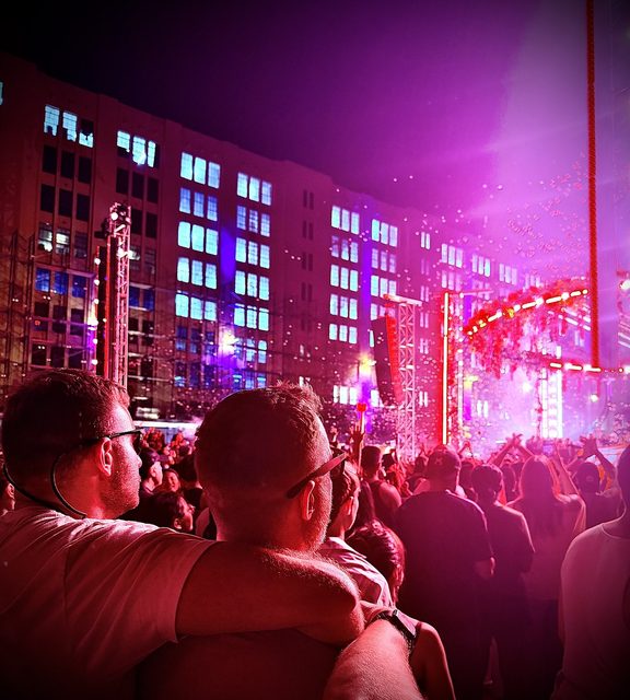 Two men seen from behind at an outdoor concert lit in pink