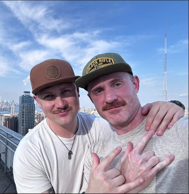 Derek and Sean on a rooftop with the skyline behind them